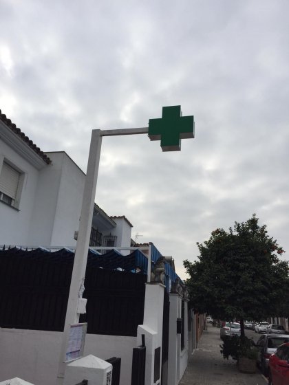 Rótulo cruz de farmacia y mástil montado sobre acerado en Sevilla.