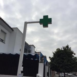 Rótulo cruz de farmacia y mástil montado sobre acerado en Sevilla.