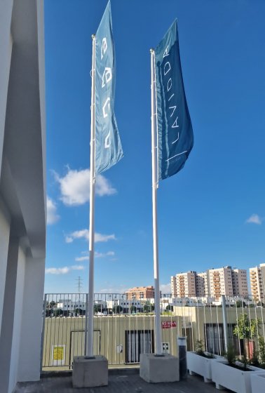 Mástil en fibra de vidrio con potencia y banderas. Dado de hormigón. Para Deacapital en Entrenúcleos Dos Hermanas Sevilla.